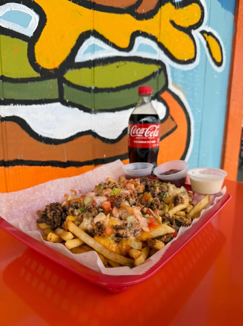 Loaded fries with ground beef, cheese, and vegetables, served with a Coca-Cola bottle.