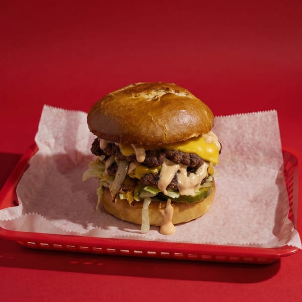 A large double cheeseburger with special sauce, lettuce, and pickles in a red basket.