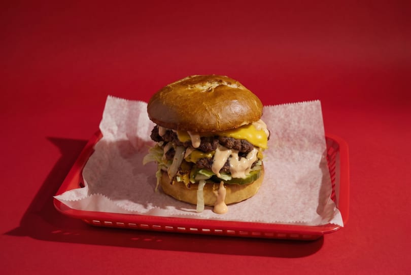 A large double cheeseburger with special sauce, lettuce, and pickles in a red basket.