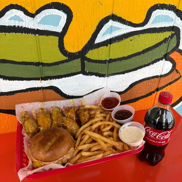 A red basket with a burger, fries, chicken wings, dipping sauces, and a Coca-Cola bottle.